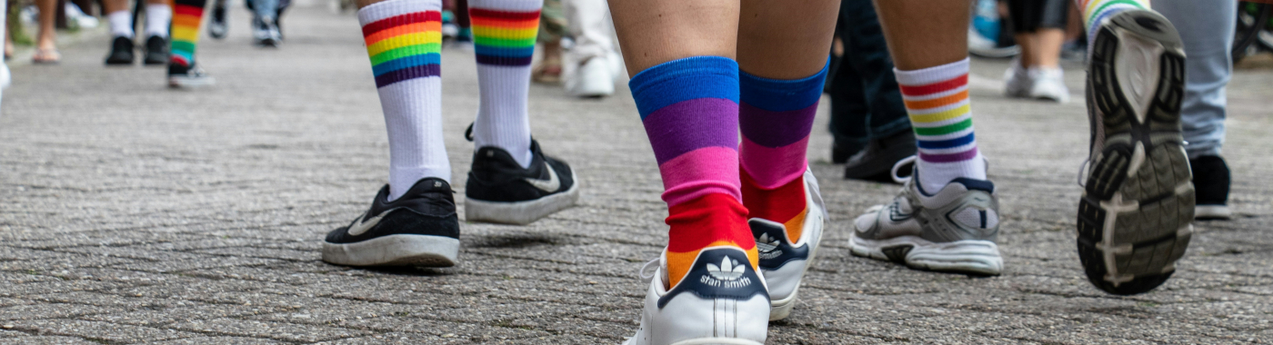 picture showing people walking on concrete from the calves down and they are wearing tennis shoes and rainbow socks.